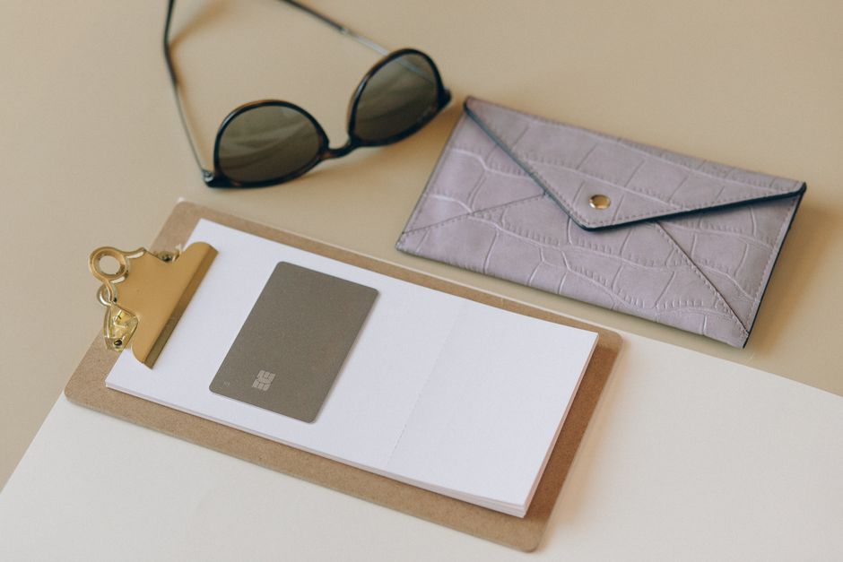 Stylish and minimalist desk setup featuring a clipboard, credit card, sunglasses, and wallet.